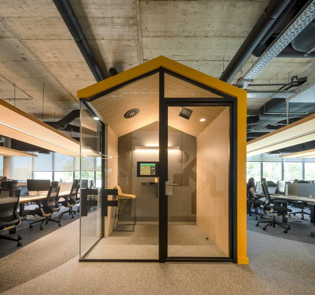 Une cabine vitrée en open space par une entreprise haut de gamme. Intérieur bois, toit incliné.