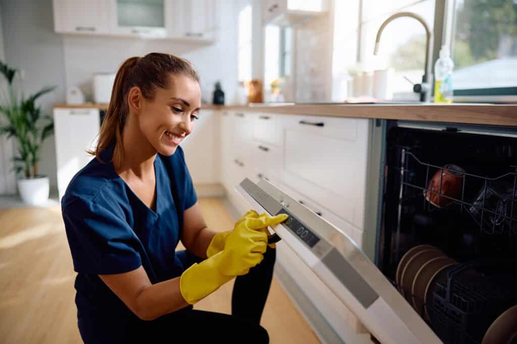 Une femme souriante ferme un lave-vaisselle moderne.